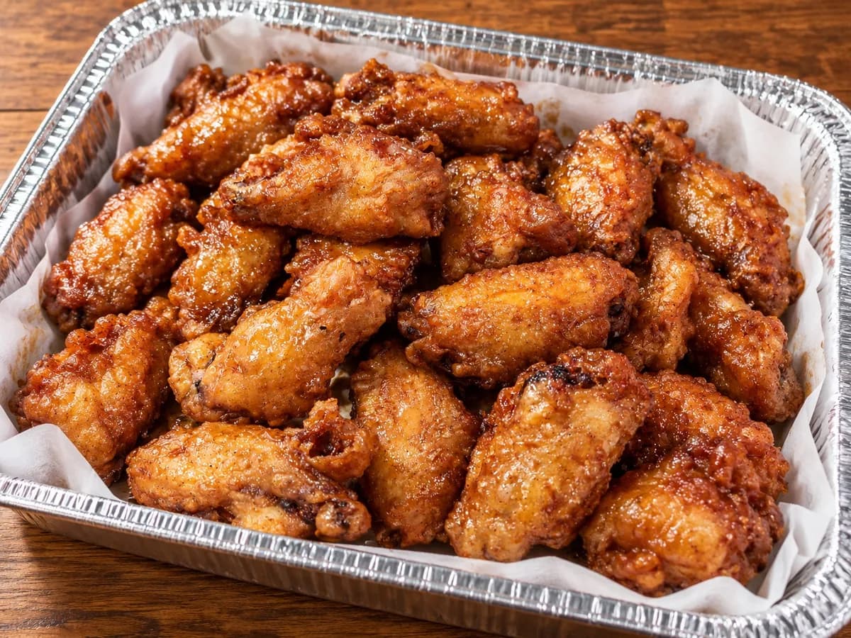 A catering tray filled with glazed chicken wings